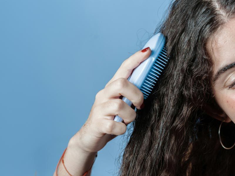 A person brushing their curly, frizzy hair in front of a blue background