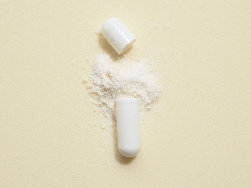 An opened pill capsule with powder spilling out on a light green surface