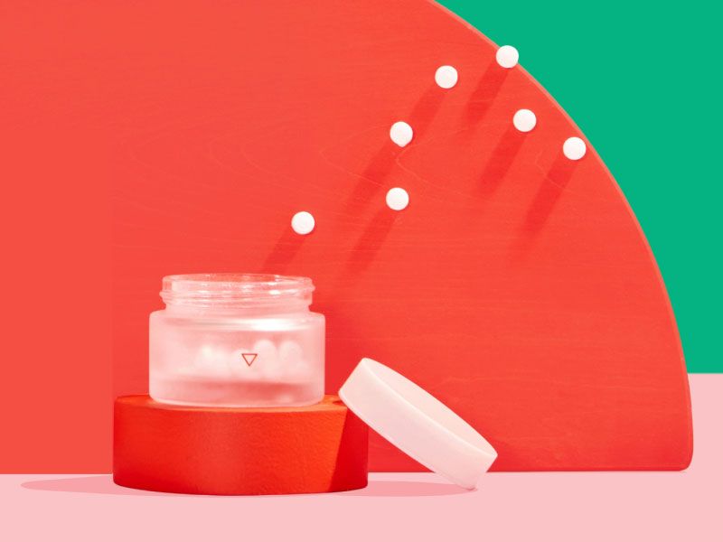 Wisp small glass pill jar with floating pills around colorful abstract shapes on a pink surface with a green background