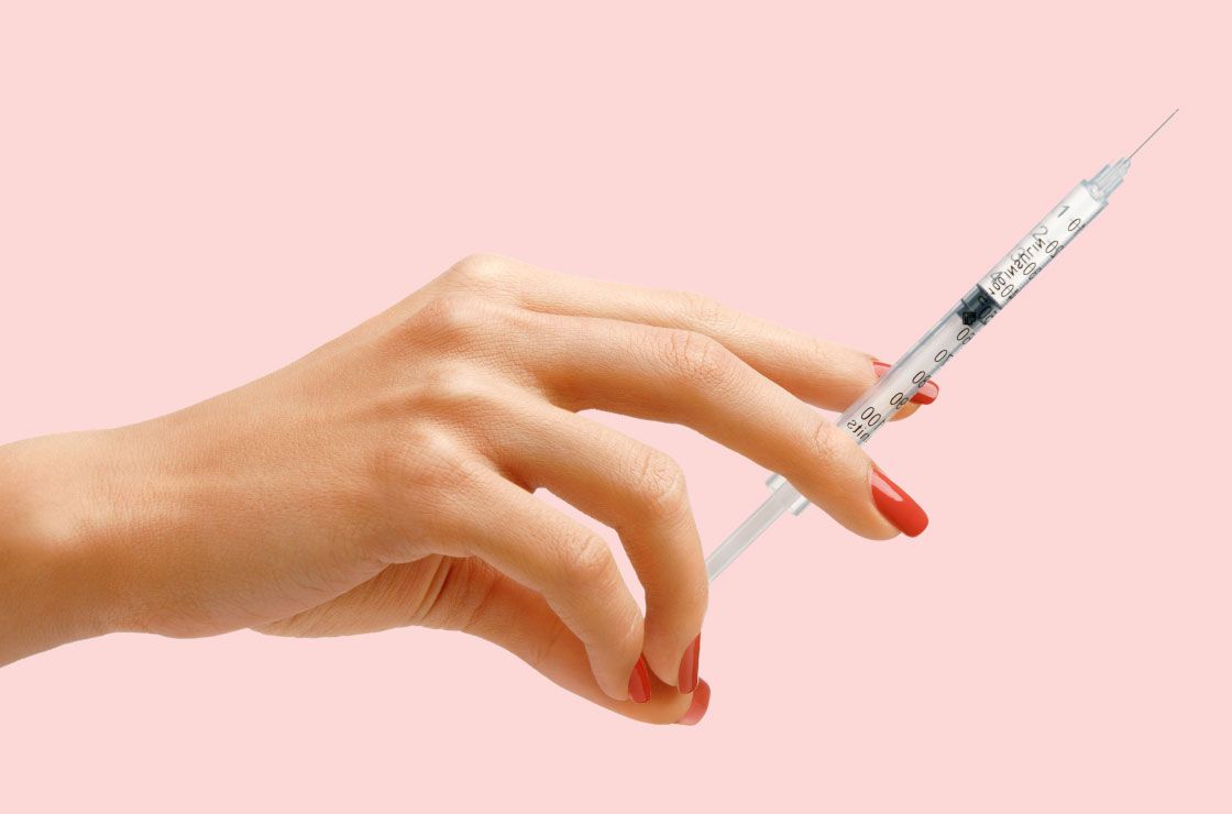 A woman's hand holding a syringe in front of a pink background