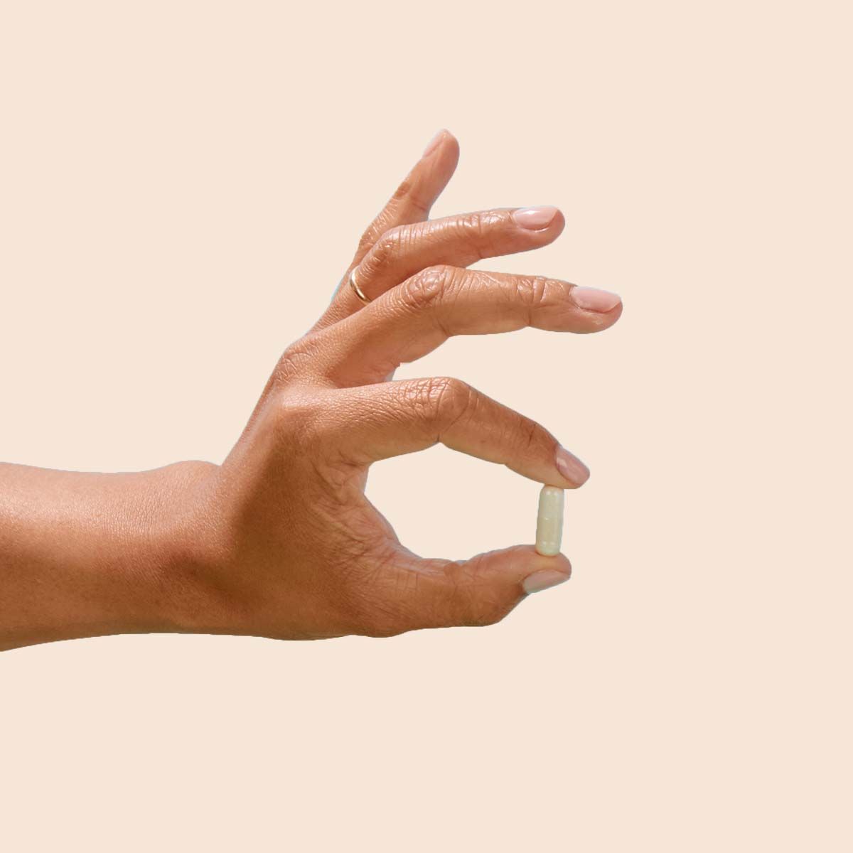 A woman's hand holding a capsule in front of a cream background