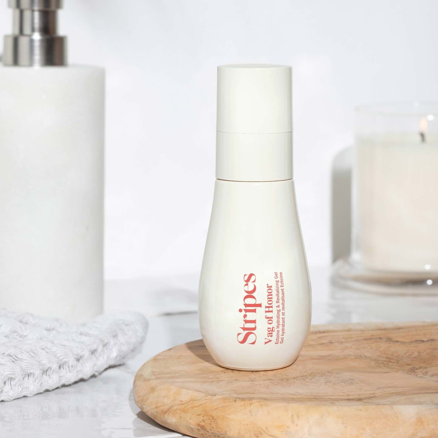 A bottle of Vag of Honor by Stripes Beauty on a countertop with soap and a candle