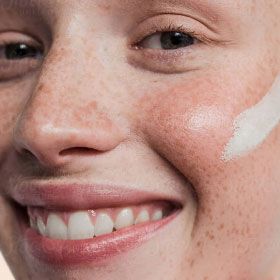 A smiling woman with freckles and a swipe of cream on her cheek