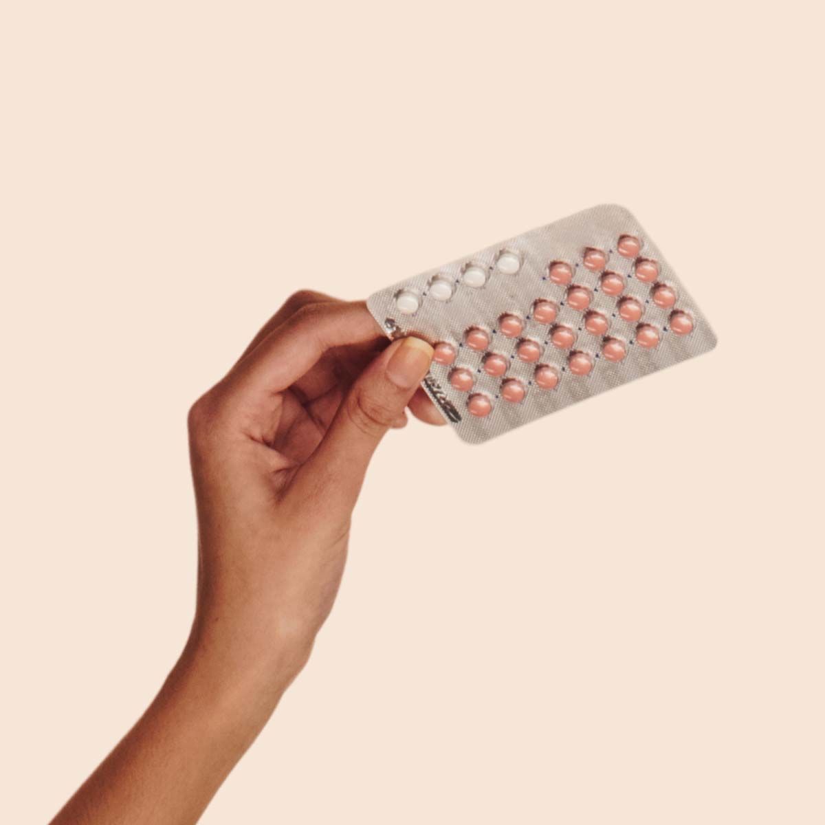 Birth Control Packet in a person's hand with a cream background