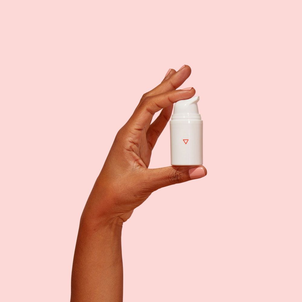 A woman's hand holding a Wisp pump bottle in front of a pink background