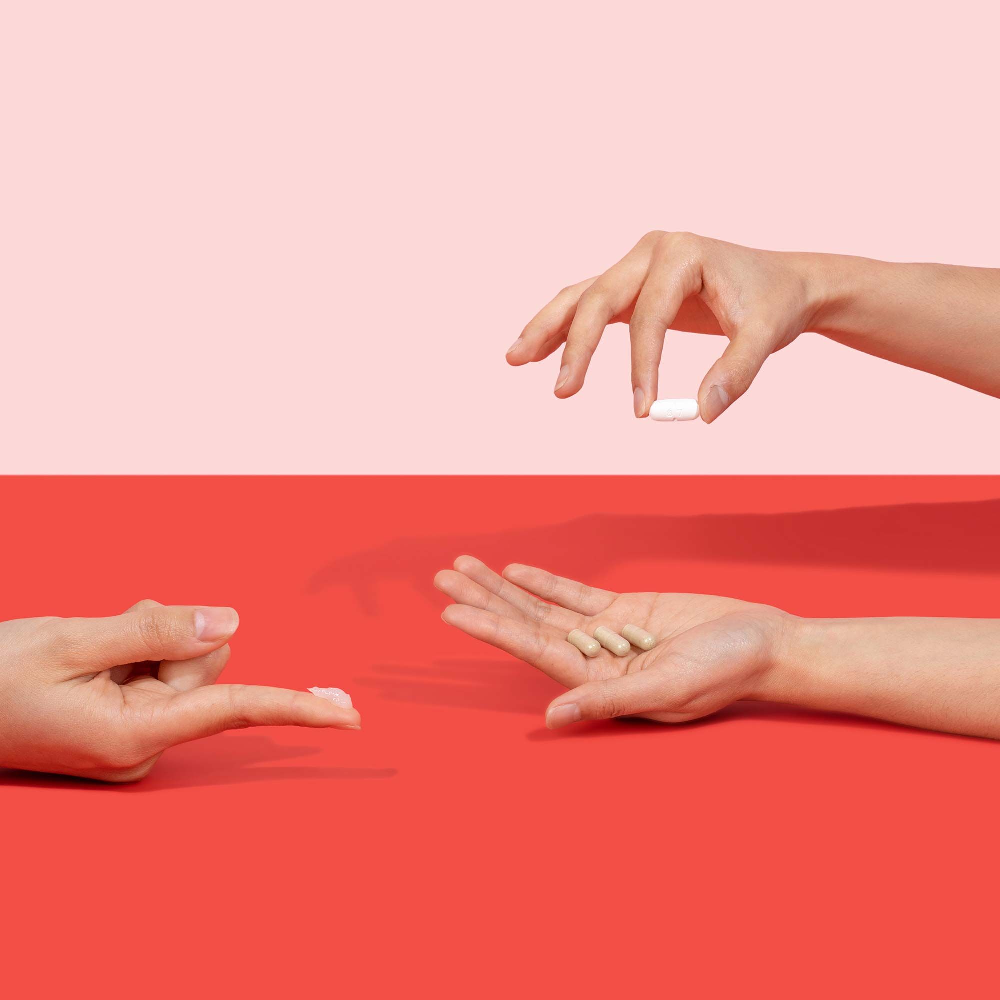 Two people's hands holding Herpes treatment pills and a swatch of cream on their fingertip on a red surface with a pink background