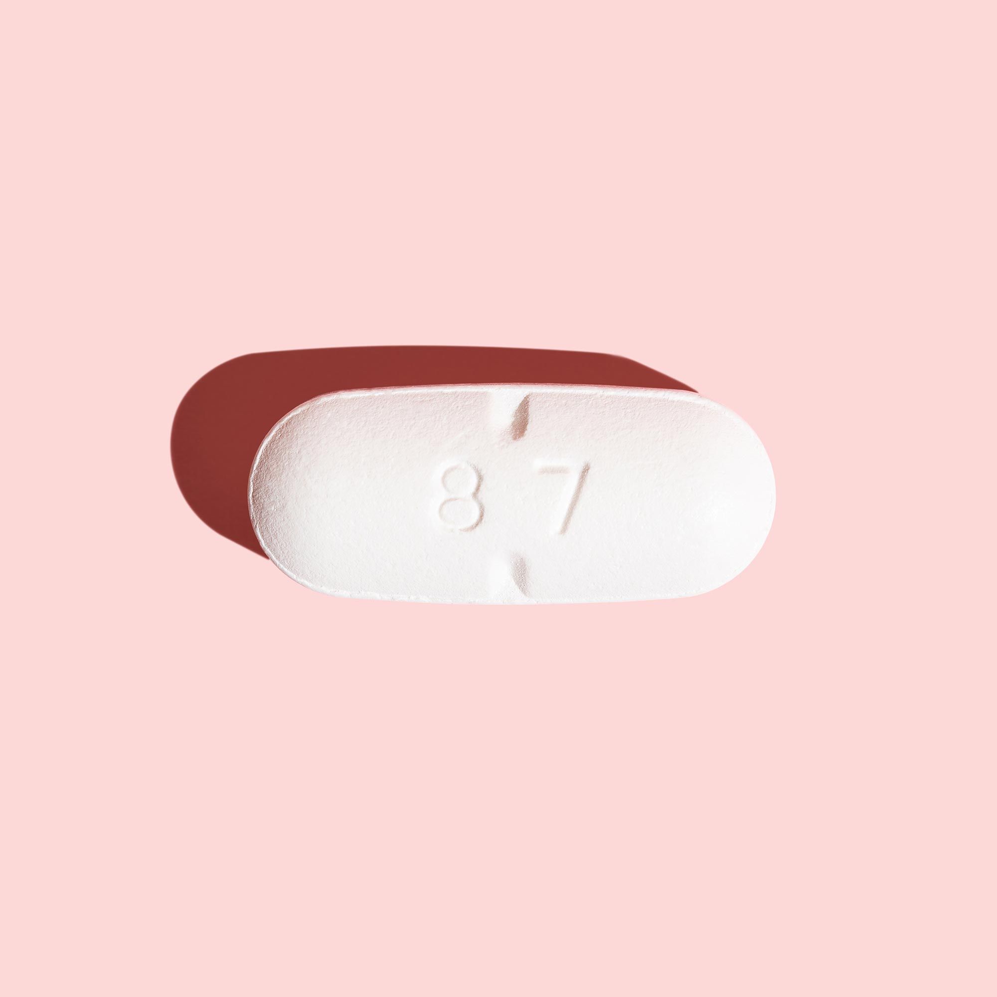A white antiviral pill on a pink surface