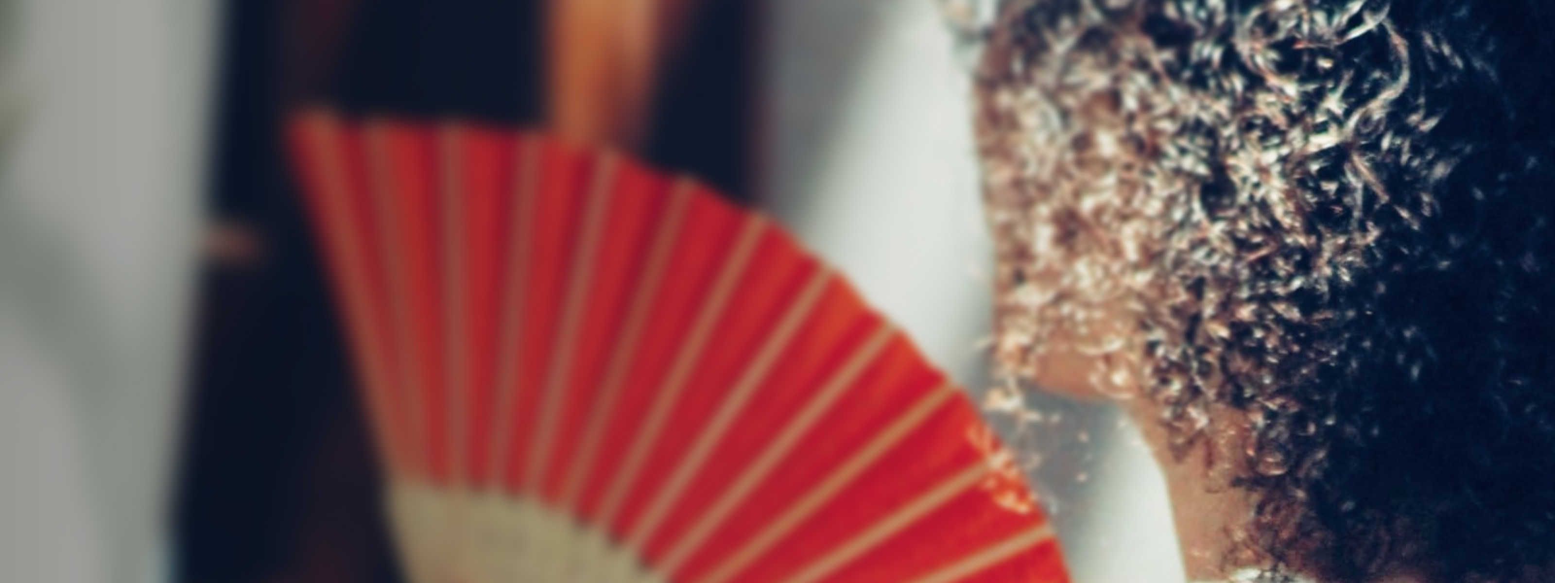woman with curly hair holding a red hand feathered fan