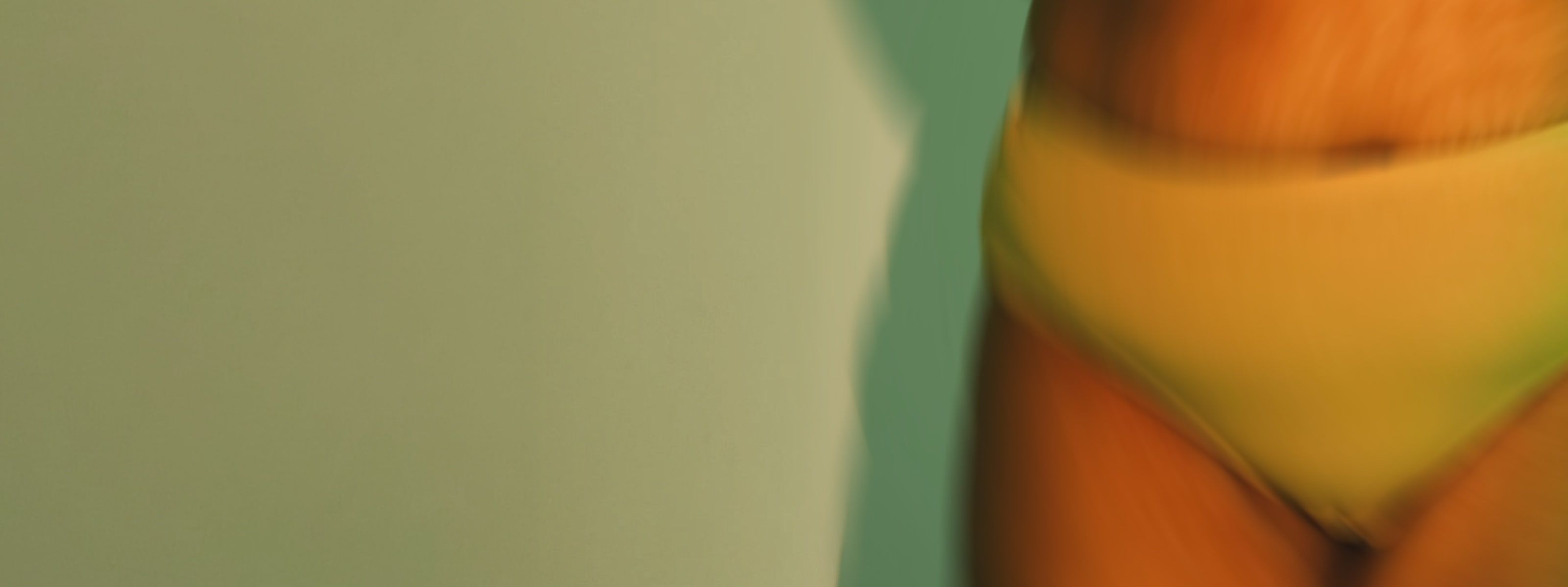 A close-up of a person's midsection wearing yellow bikini bottoms against a teal background.