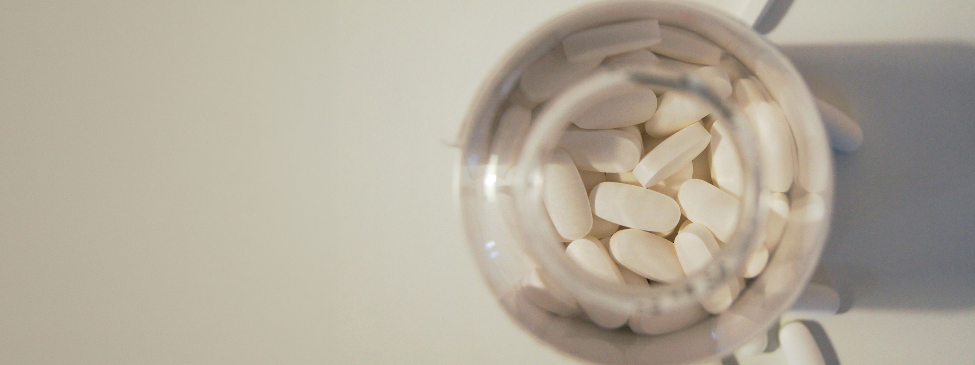 Open bottle filled with white oval tablets viewed from above