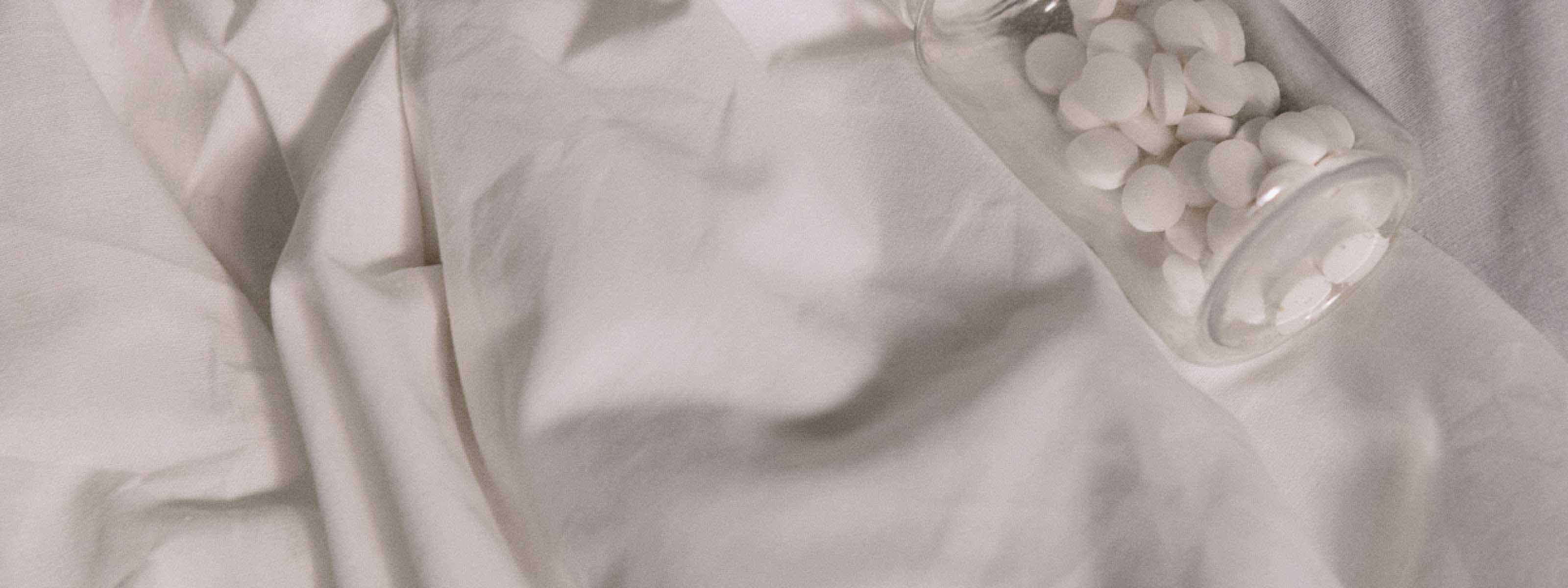 A clear bottle of round white pills on white bedding