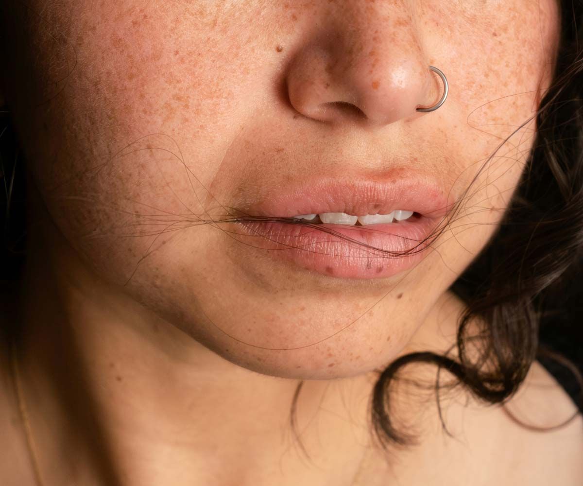 A close up of a woman's face with dark hair and a nose piercing