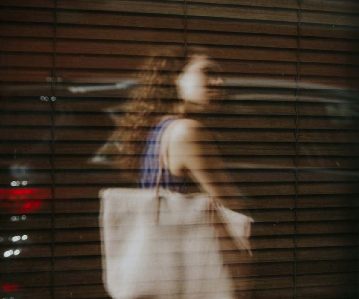 A woman with curly hair carrying a tote in the city with motion blur