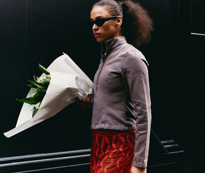 woman walking with jacket and sunglasses on holding a bouquet of flowers wrapped in white paper