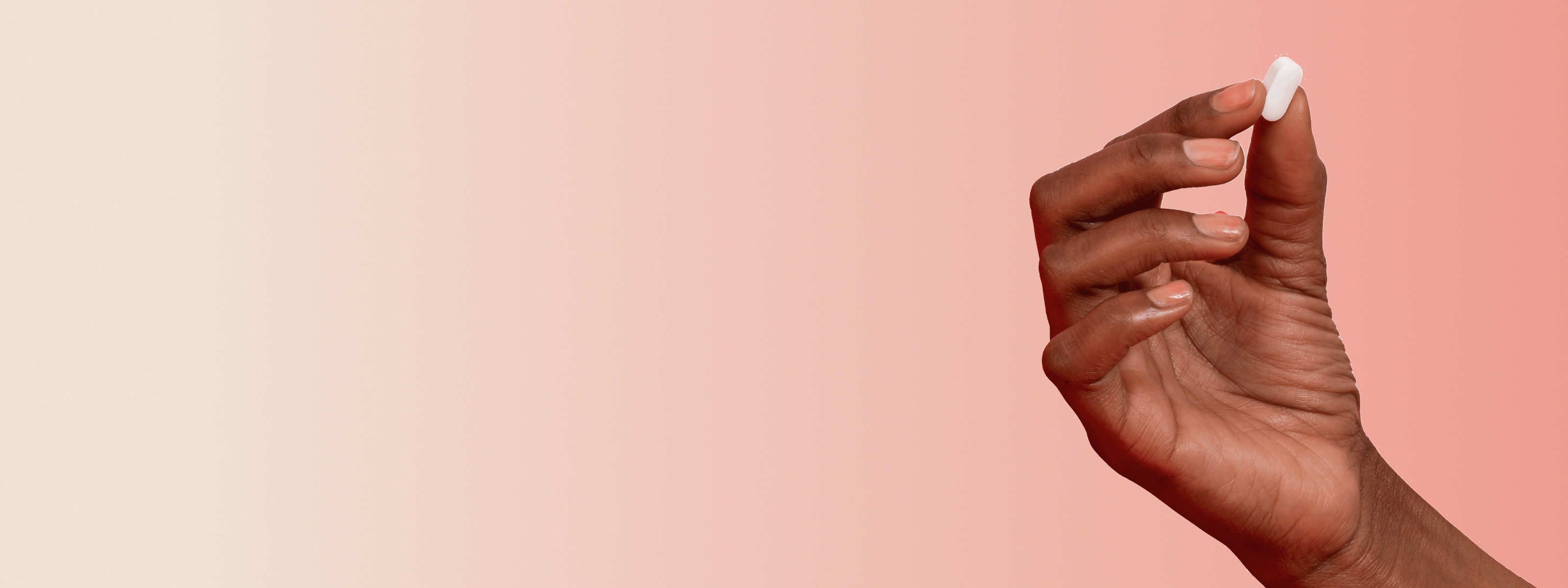 hand holding a white pill in front of an orange beige background
