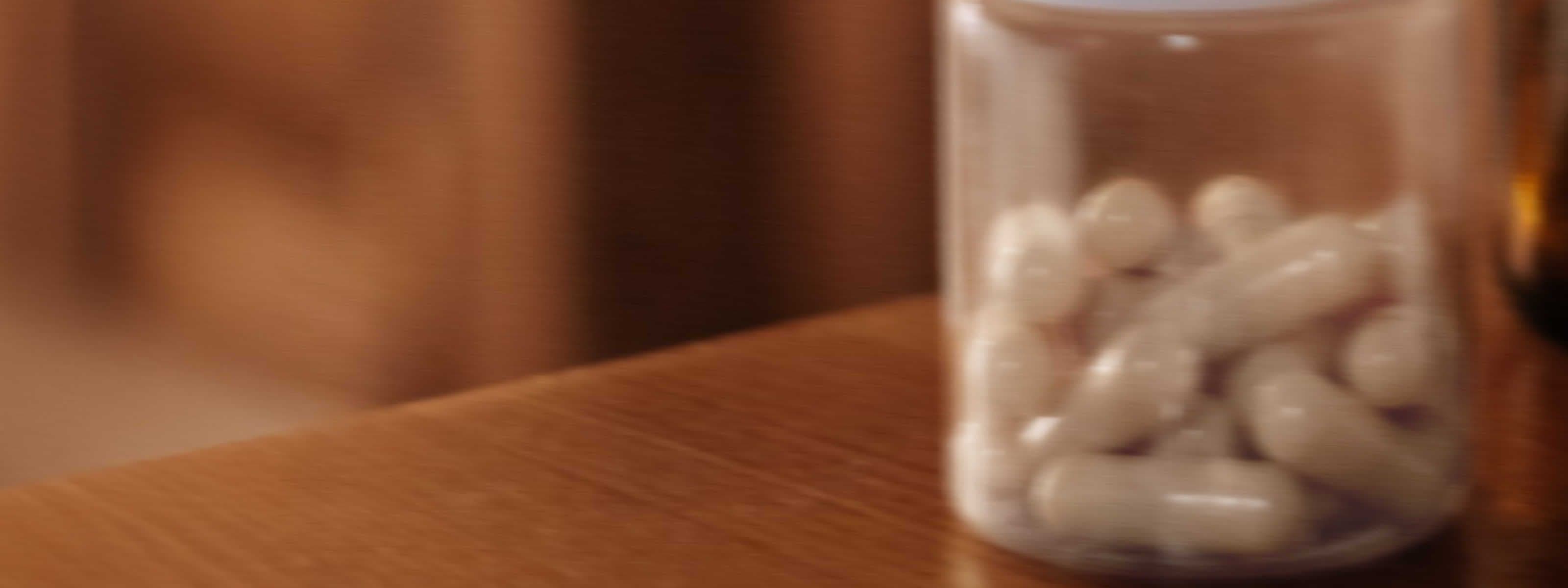 image of a clear, blurry bottle with white capsules on a brown wooden desk