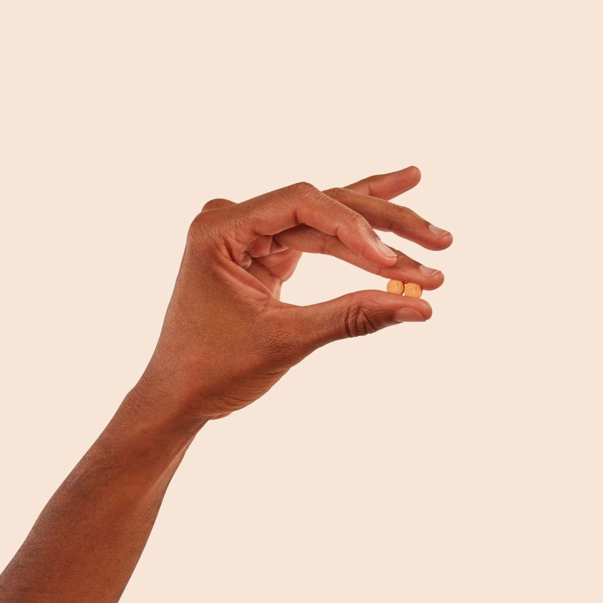 A person's hand holding two DoxyPEP pills with a cream background