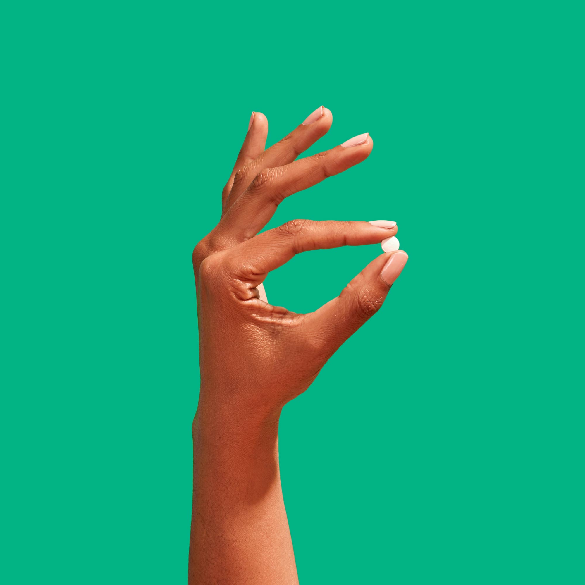 Hand holding Ella emergency contraception pill to prevent pregnancy on a green background