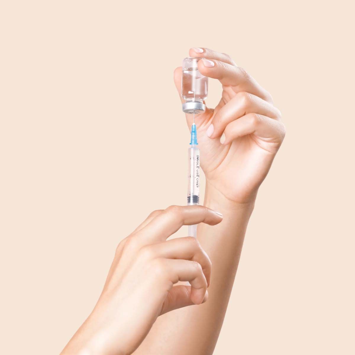 A person's hands filling a syringe with liquid from a vial in front of a cream background