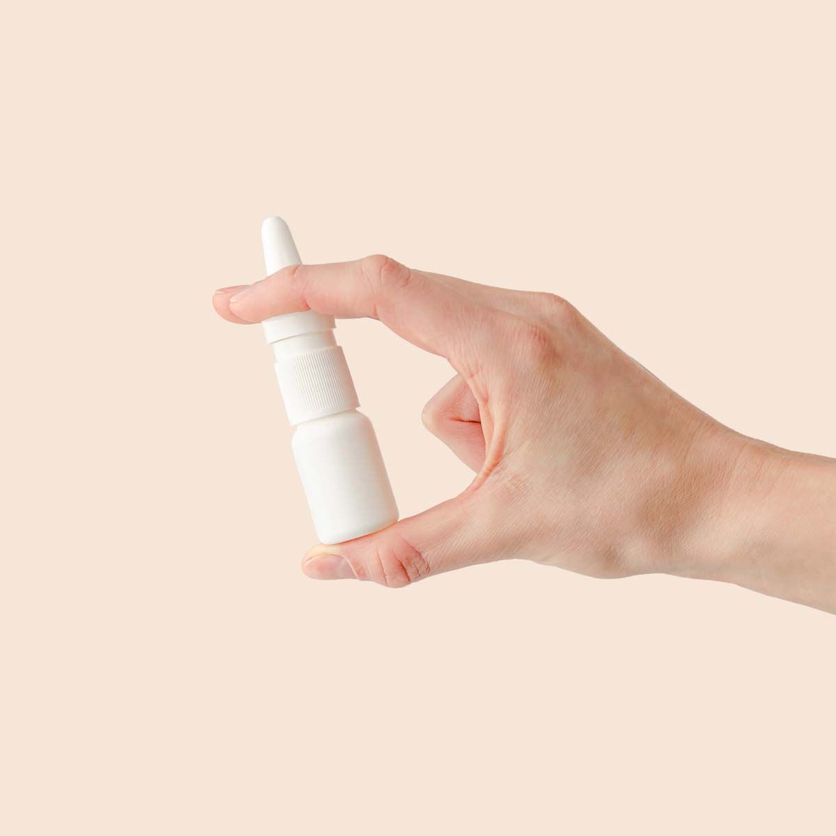 A hand holding a nasal spray bottle in front of a cream background