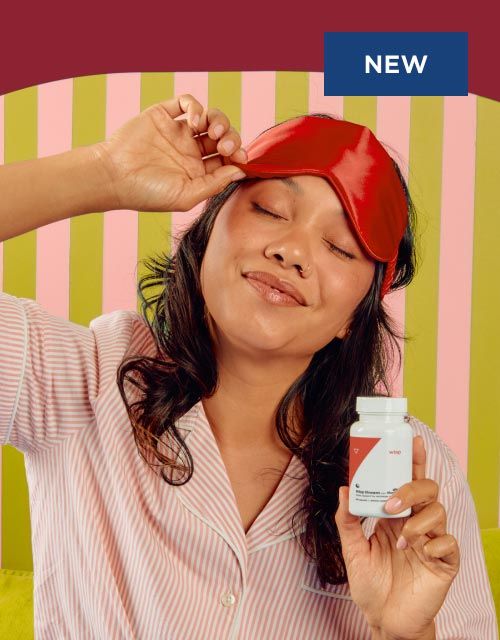 A woman wearing pajamas and a sleep mask is holding a bottle of Wisp Dream Sleep Aid