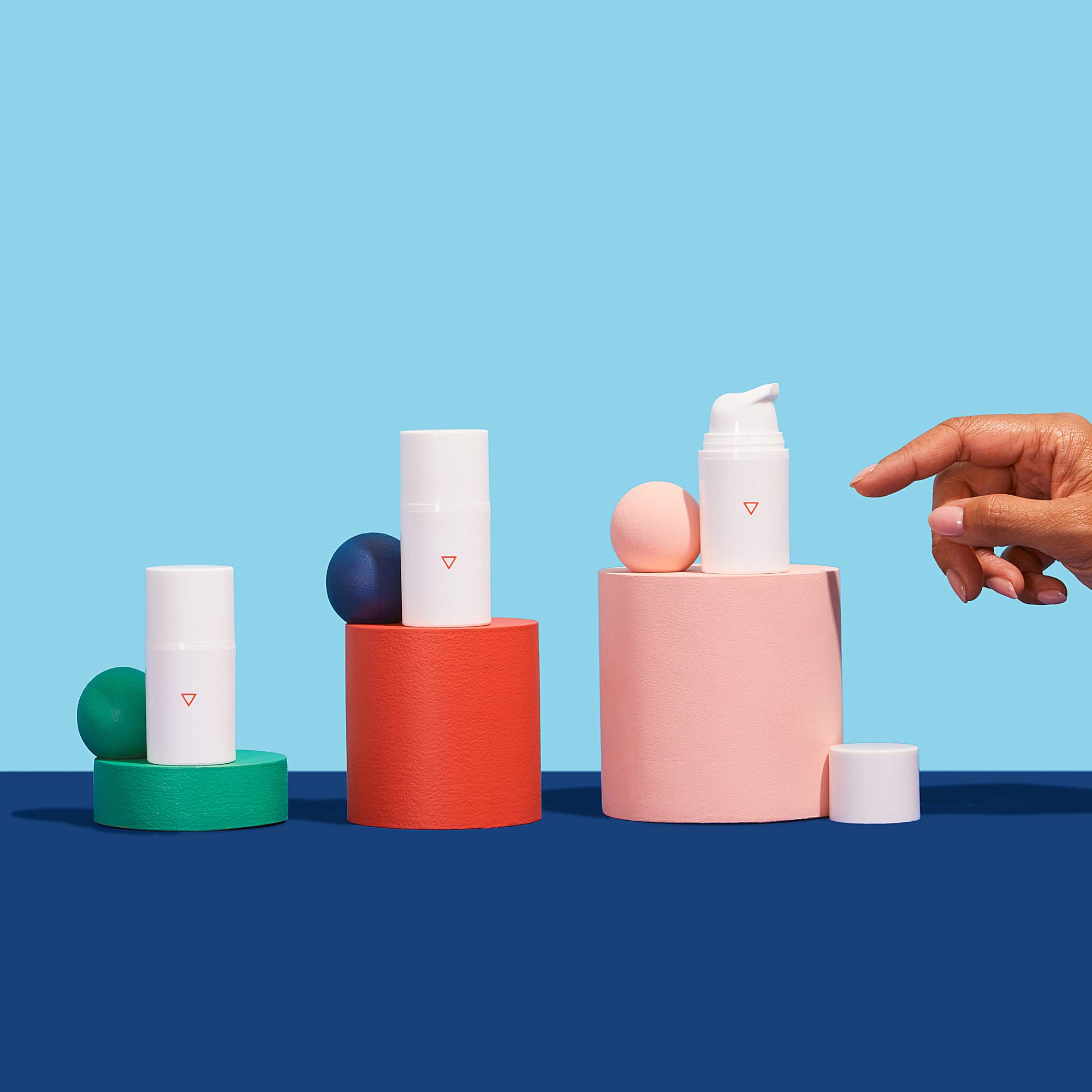 A woman's hand reaching for 3 bottles of Wisp Hydrocortisone Cream balancing on colorful abstract shapes on a blue surface