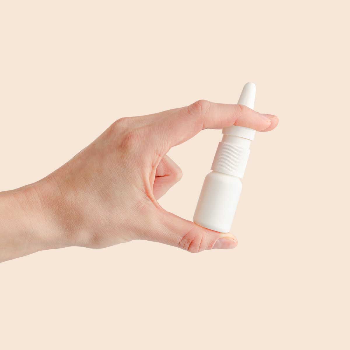 A person's hand holding a nasal spray bottle with a cream background