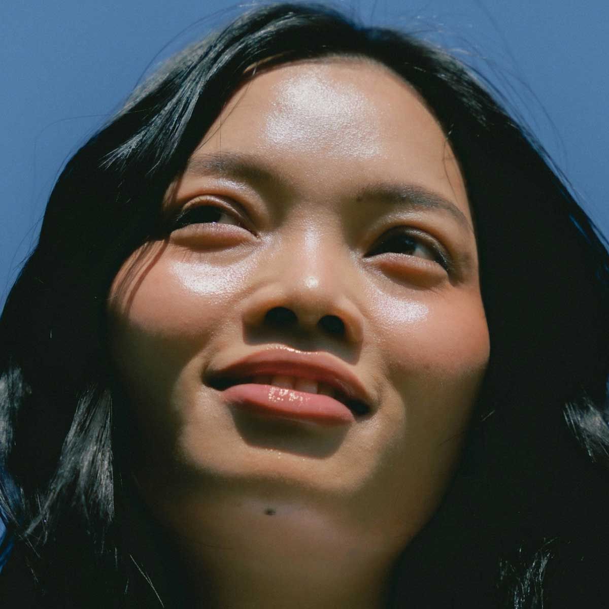 A smiling woman with glowing skin and a blue sky in the background