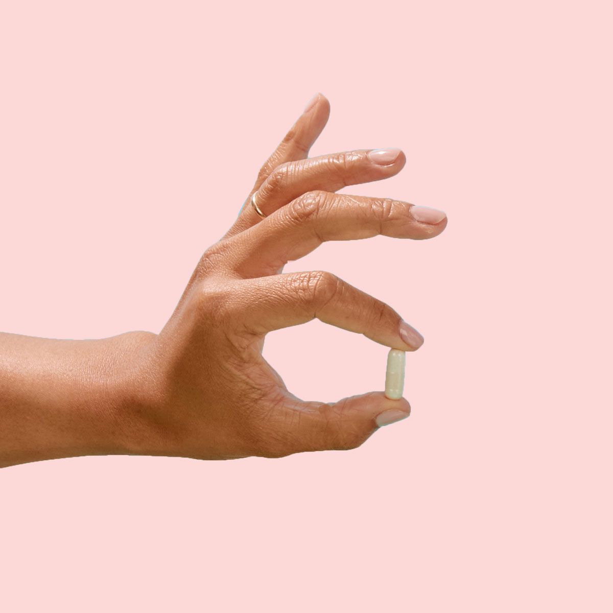 A woman's hand holding a capsule in front of a pink background