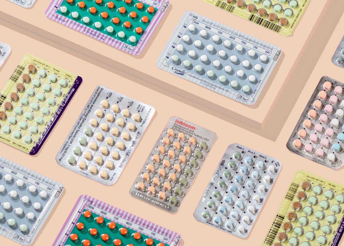A flatlay of multiple birth control packets with colorful abstract shapes on a cream surface
