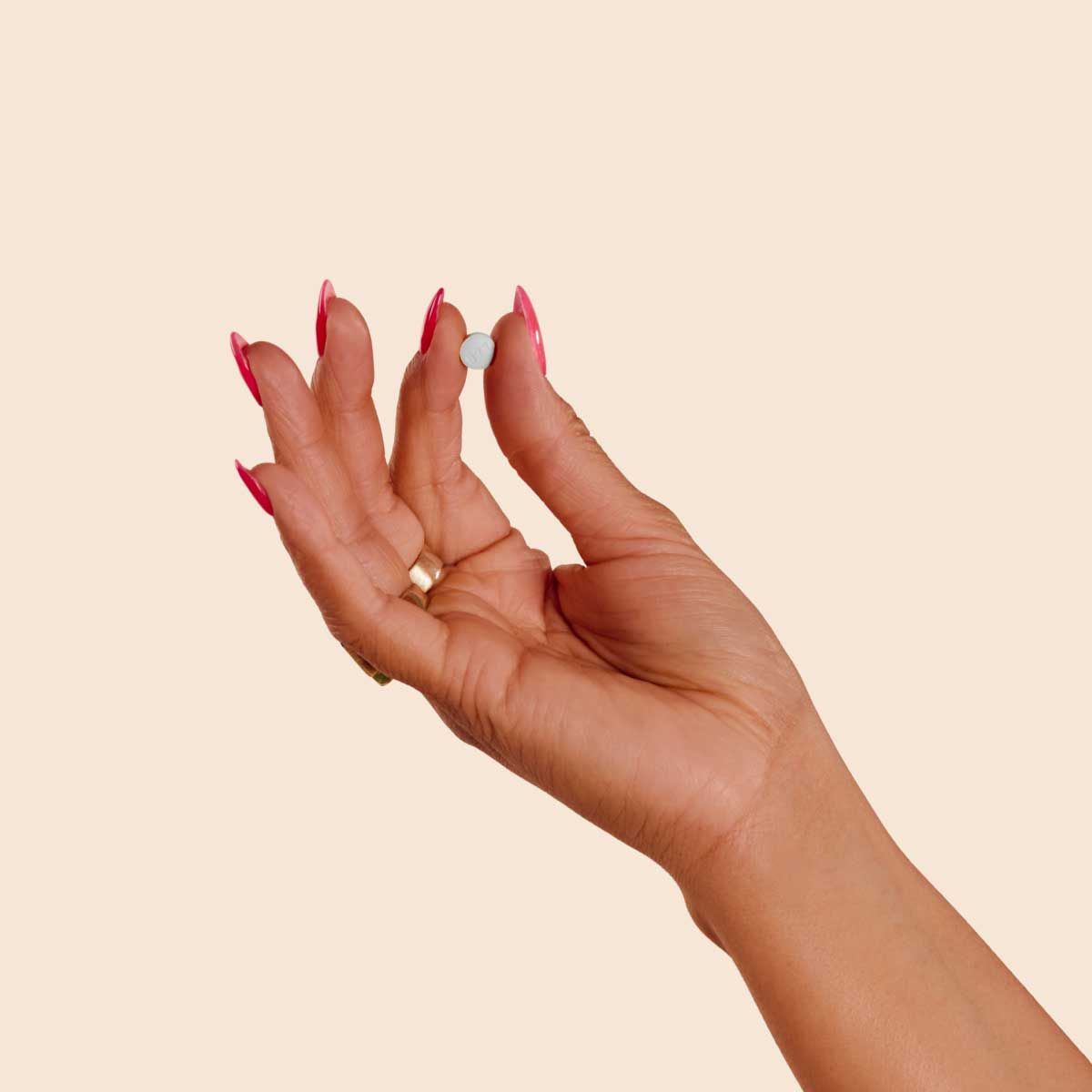 A woman's hand holding a small white round pill with a cream background