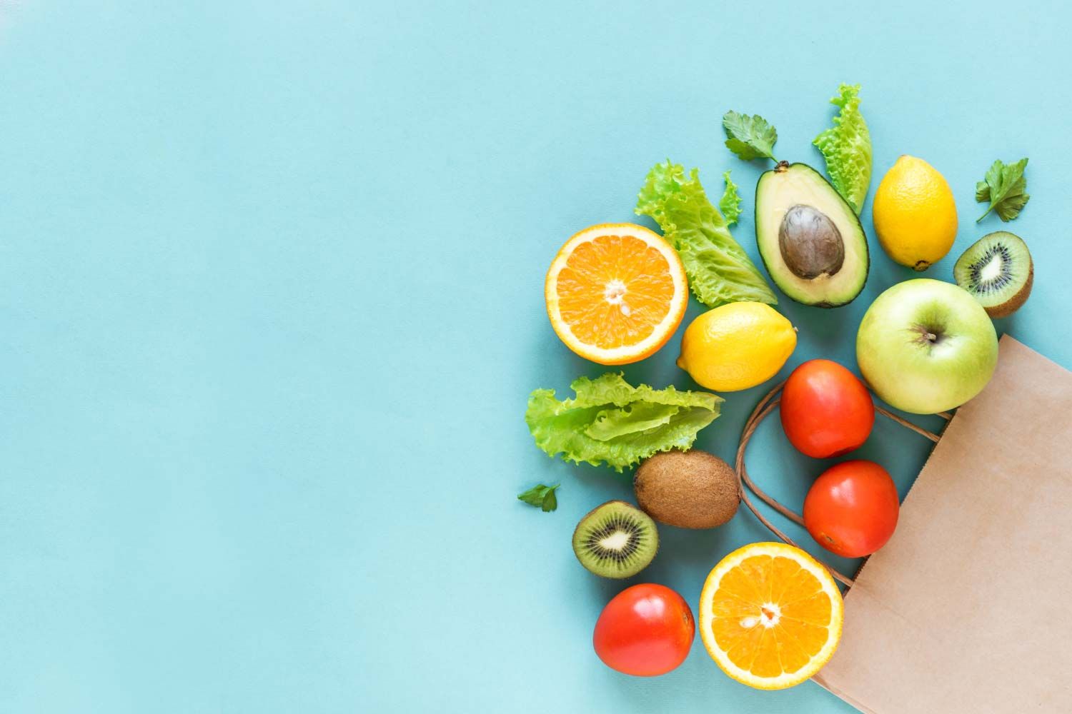 A grocery bag with healthy vegetables and fruits laid out on a light blue surface