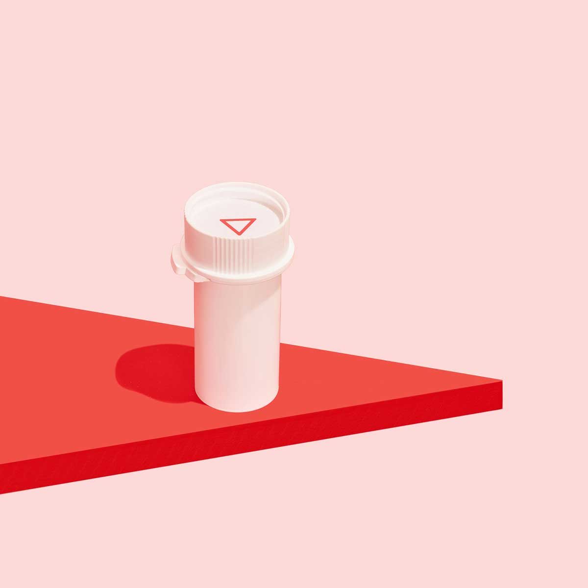 A Wisp pill vial on a red surface with a pink background