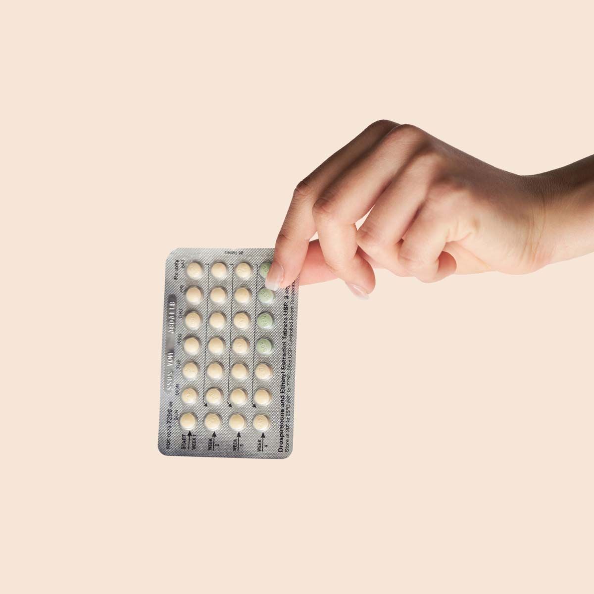 A person's hand holding Microgestin birth control on a cream surface