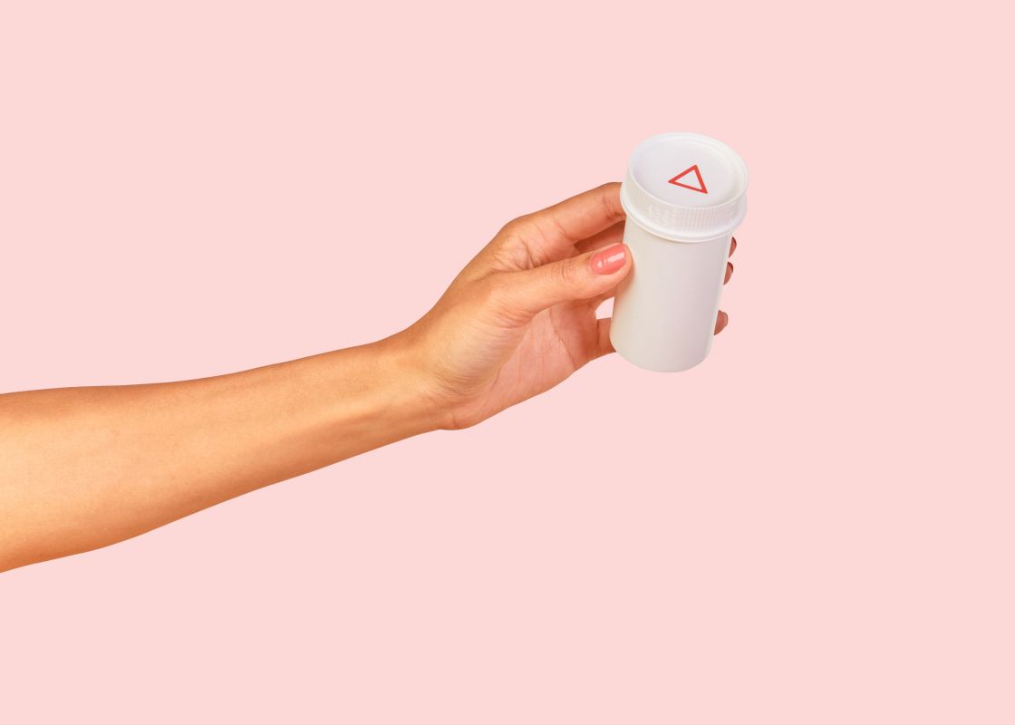 a woman's hand holding a Wisp prescription vial with migraine treatment on a pink background