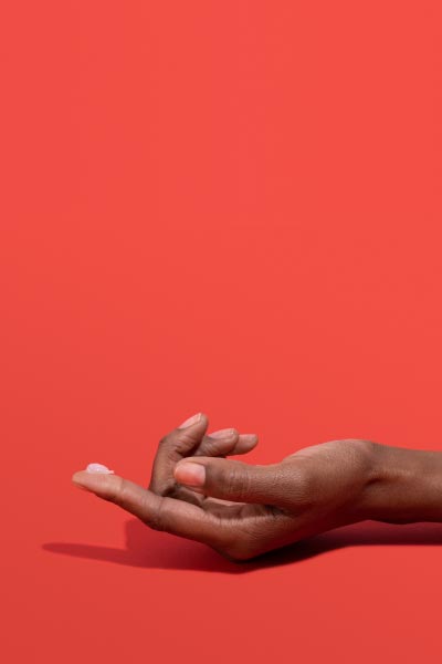 A woman's hand with Acyclovir Cream on the index finger and a red background