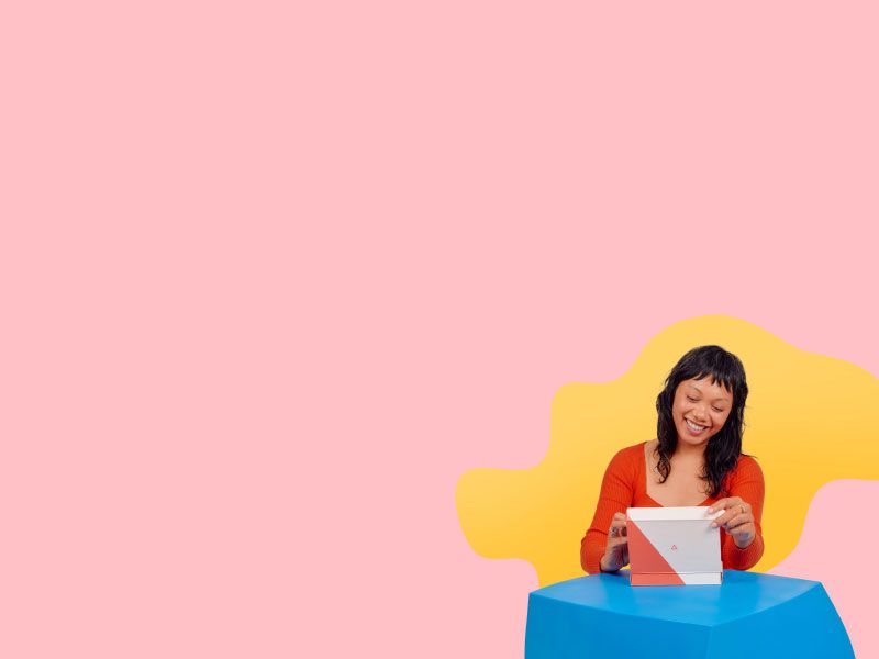 A smiling woman wearing a red top is opening a Wisp Diagnostics package on a blue table