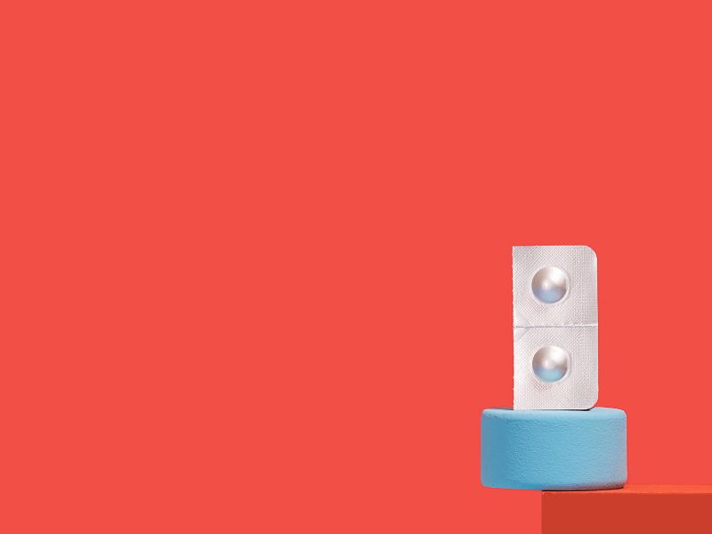 A pill packet of Zofran balanced on colorful abstract shapes in front of a red background