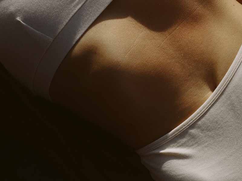 Close-up of a stomach and chest in a white tank top and shorts with warm, dramatic sunlight.