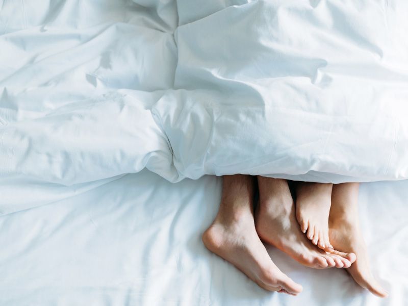 A couple's feet sticking out from underneath a white comforter