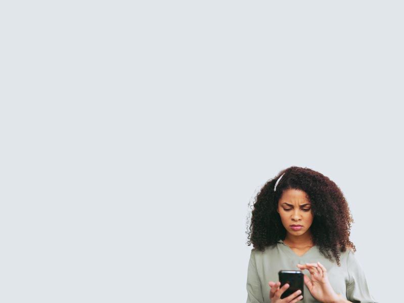 A woman wearing a gray shirt is looking at a mobile phone with a confused expression on her face
