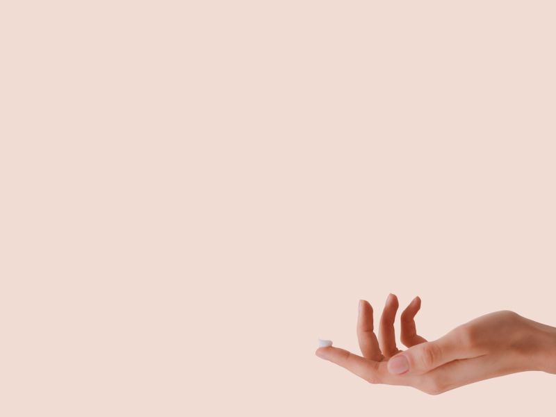 A hand with cream on the index finger tip with a beige background