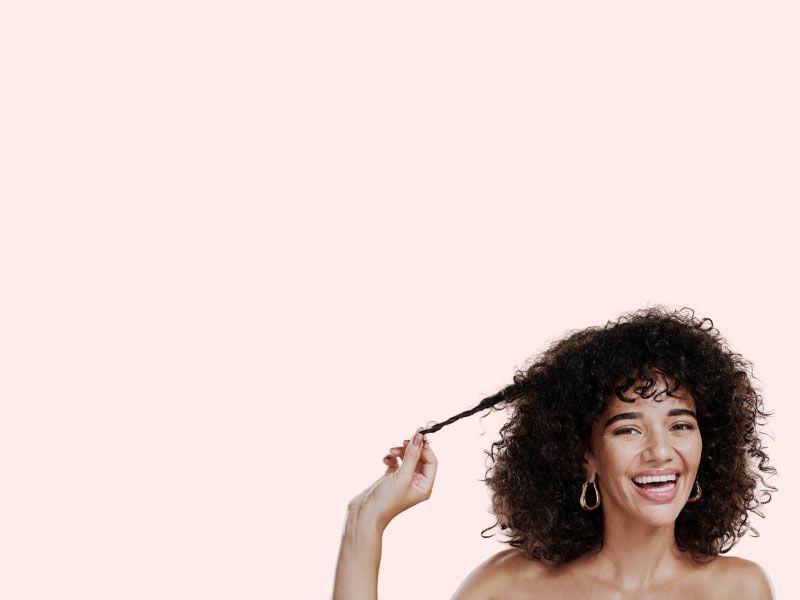 A smiling woman with luscious thick curly hair in front of a peach-colored background