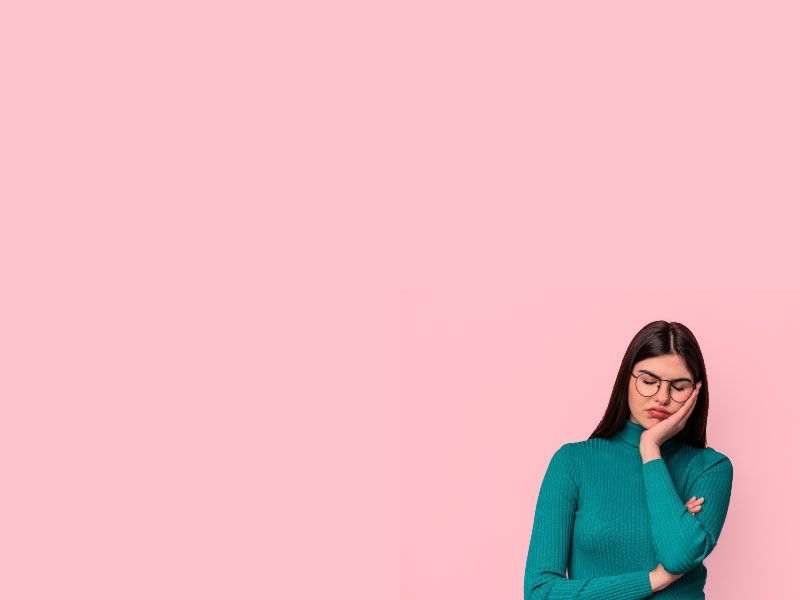 A woman wearing a green sweater and looking tired in front of a pink background