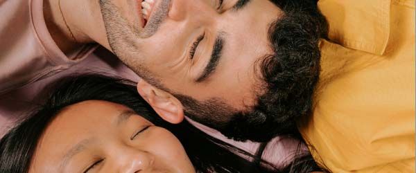 Two women and a man wearing colorful clothes while laying on their back and smiling