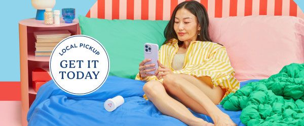 A woman laying on a bed with colorful bedding using a mobile phone next to a nightstand with Wisp medication bottles