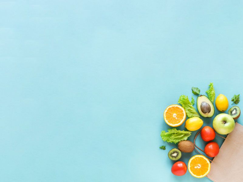 A grocery bag with healthy vegetables and fruits laid out on a light blue surface