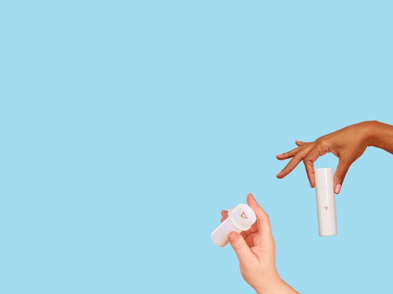 Two people's hands holding a Wisp pill vial and a Wisp pump bottle in front of a light blue background