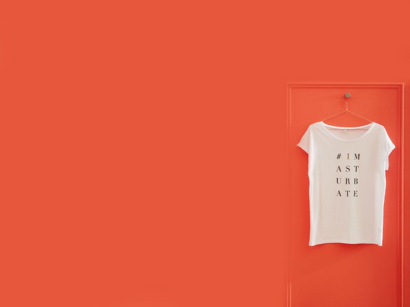 A white shirt hanging on an orange wall that says #IMASTURBATE on it