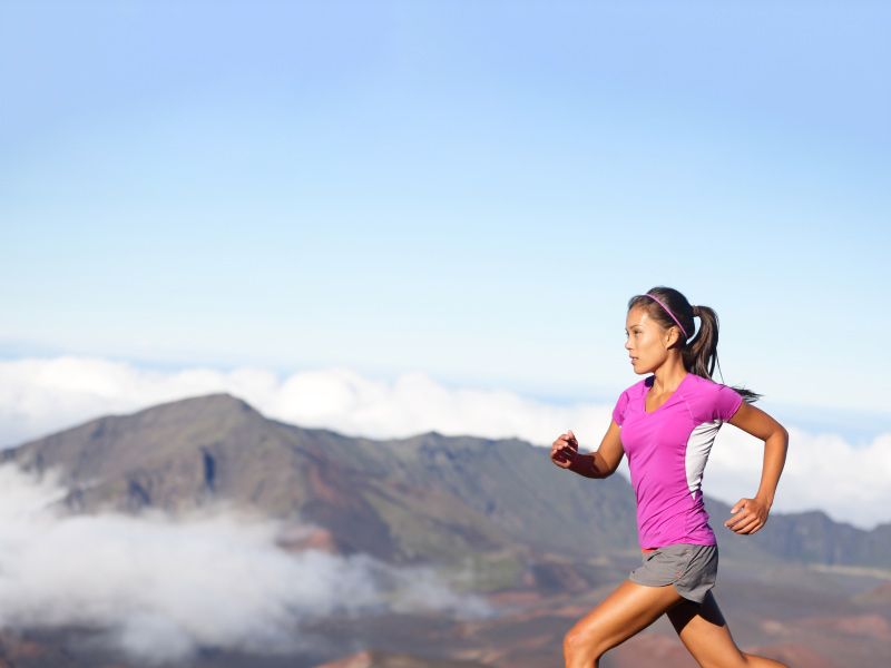 a woman in a pink shirt trail running under blue skies with mountains in the background